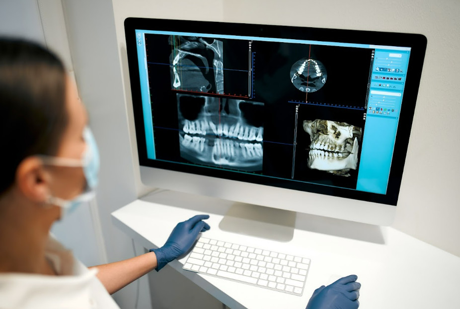 Dentist reviewing CBCT slices and a 3D jaw reconstruction in diagnostic software on a monitor.