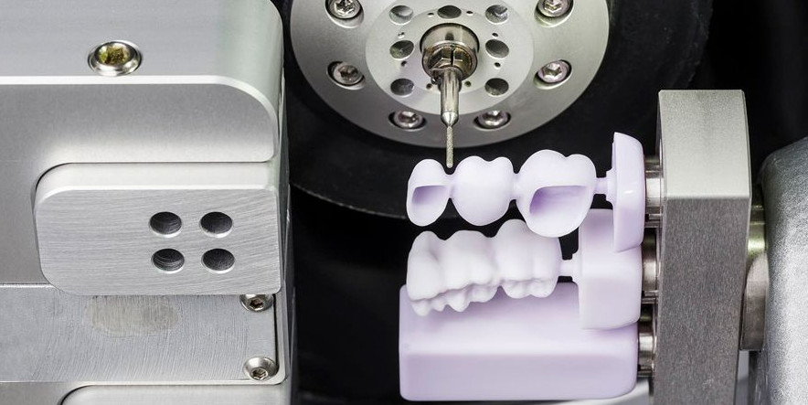 Dental milling machine carving a three-unit bridge from a ceramic blank inside the milling chamber.